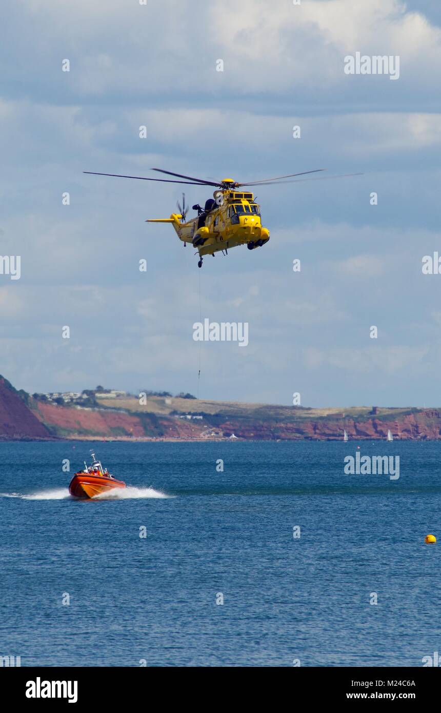 Air Sea Rescue Training mit gelben Sea King Hubschrauber und RNLI Rigid Inflatable Boat. Dawlish, Devon, Großbritannien. Stockfoto