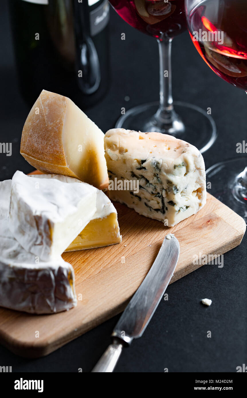 Auswahl an Käse auf einer Holzplatte mit Vintage silver Messer und zwei Gläser Rotwein. Vertikale. Stockfoto
