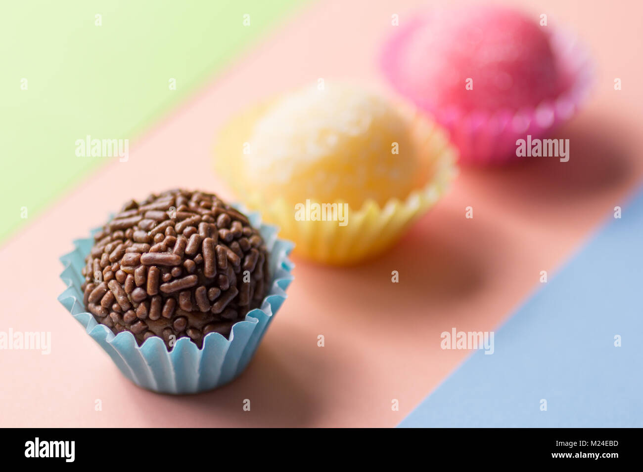 Brasilianische Spezialitäten: Brigadeiro, Beijinho und Bicho de Pe. Kindergeburtstag. Candy Balls in gerader Linie. Bunter Hintergrund. Stockfoto