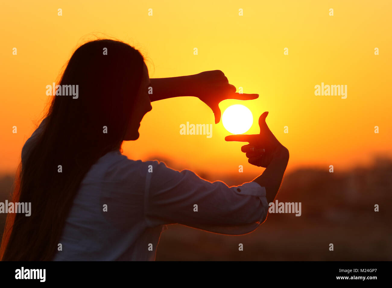 Hintergrundlicht Porträt einer Frau Silhouette framing Sun mit den Fingern bei Sonnenuntergang Stockfoto