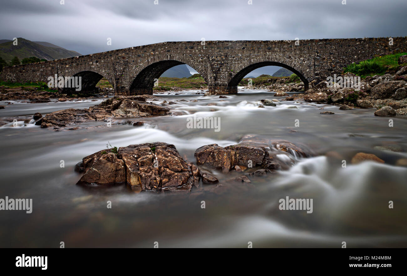 Sligachan Alte Brücke auf Scotlands Isle of Skye. Das Wasser weich mit der langen Belichtungszeit, Granitfelsen Farbe in den grauen bewölkten Tag hinzufügen. Stockfoto