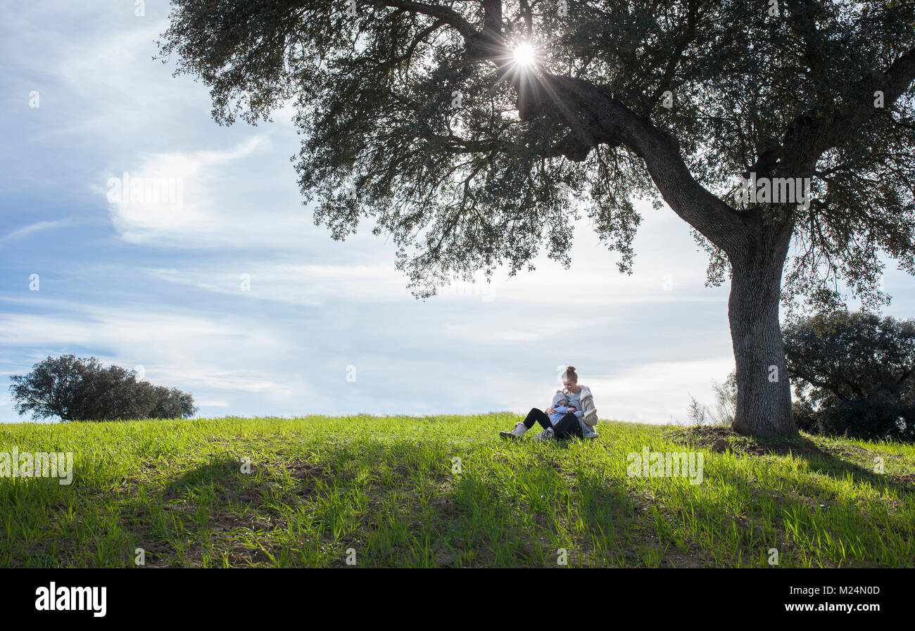 Mutter stillen Toddler boy unter dem Baum des Lebens. Erweiterte Stillen in der Natur Konzept Stockfoto