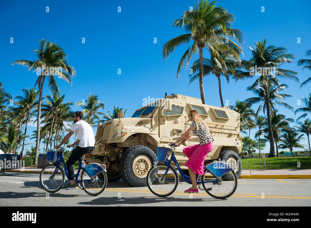 MIAMI - Dezember 29, 2017: Radfahrer fahren Sie an einem großen gepanzerten Militärfahrzeugen am Ocean Drive als Sicherheit stationiert für Urlaub feiern erhöht wird. Stockfoto