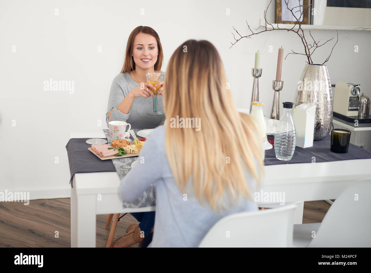 Lächelnde Frau mit Frühstück mit ihrer Tochter oder Freundin am Tisch sitzen mit einem gesunden Verbreitung von Obst, Müsli, Brötchen, Aufschnitt, Käsesorten Stockfoto