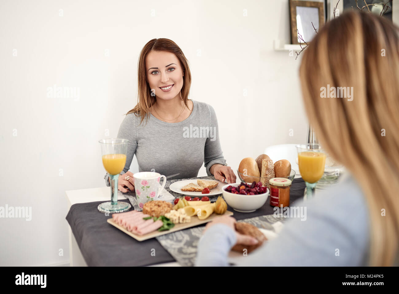 Lachelnde Frau Mit Fruhstuck Mit Ihrer Tochter Oder Freundin Am Tisch Sitzen Mit Einem Gesunden Verbreitung Von Obst Musli Brotchen Aufschnitt Kasesorten Stockfotografie Alamy