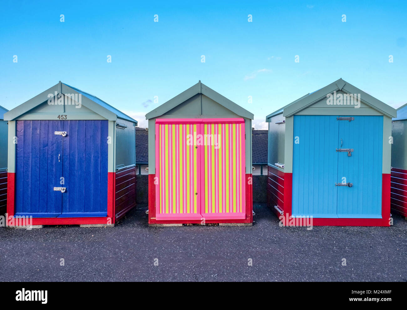 Brighton Seafront drei Kabinen, zwei mit blauen Türen und der in der Mitte hat einen bunten Tür von Gelb, Pink, Schwarz Streifen hinter ist b Stockfoto