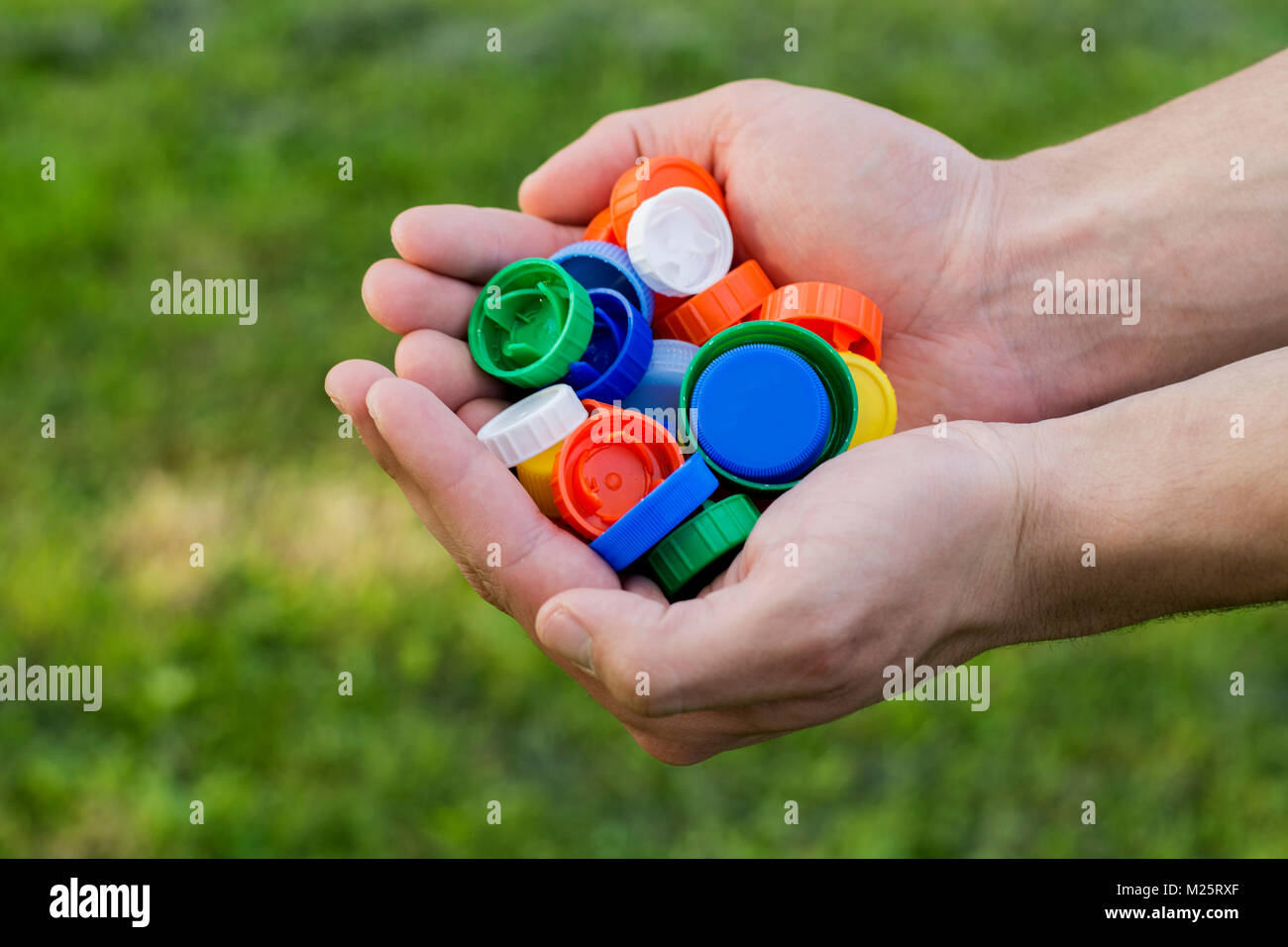 Aus recyceltem Kunststoff Verschlüsse in den Händen des Menschen. Die Rettung der Umwelt. Grüner Hintergrund Stockfoto