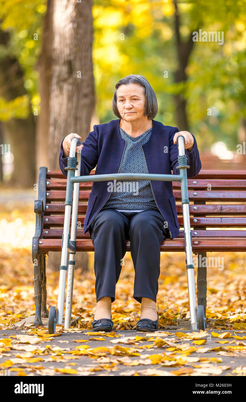 Ältere Frau mit Walker Aufstehen aus Sitzbank und Walking im Freien im Herbst Park. Stockfoto