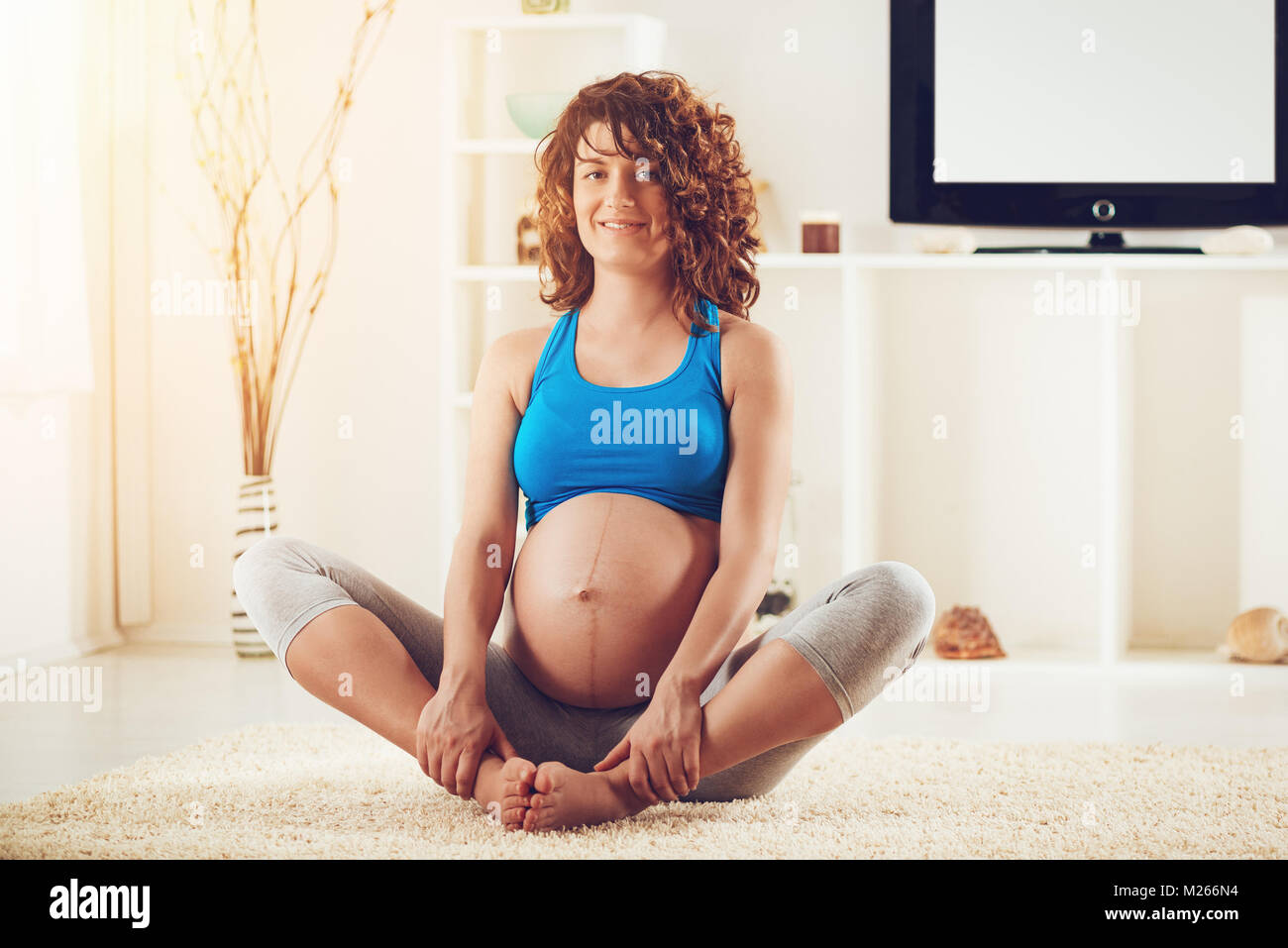 Schöne junge schwangere Frau im Hause entspannen. Sie sitzt auf dem Boden und Kamera. Stockfoto