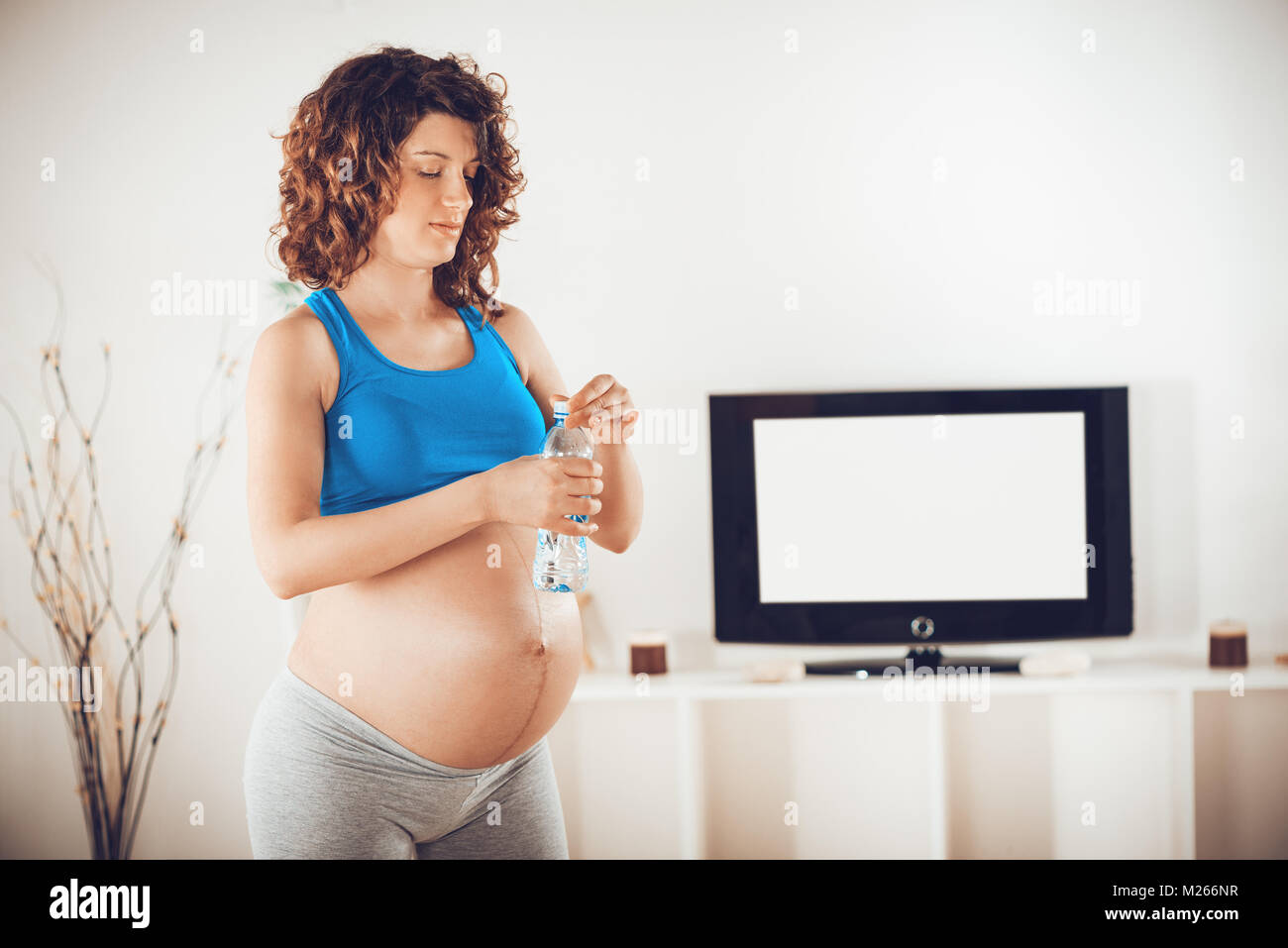 Schöne junge schwangere Frau mit einer Flasche Wasser und Relaxen im Hause nach Atemübungen. Stockfoto