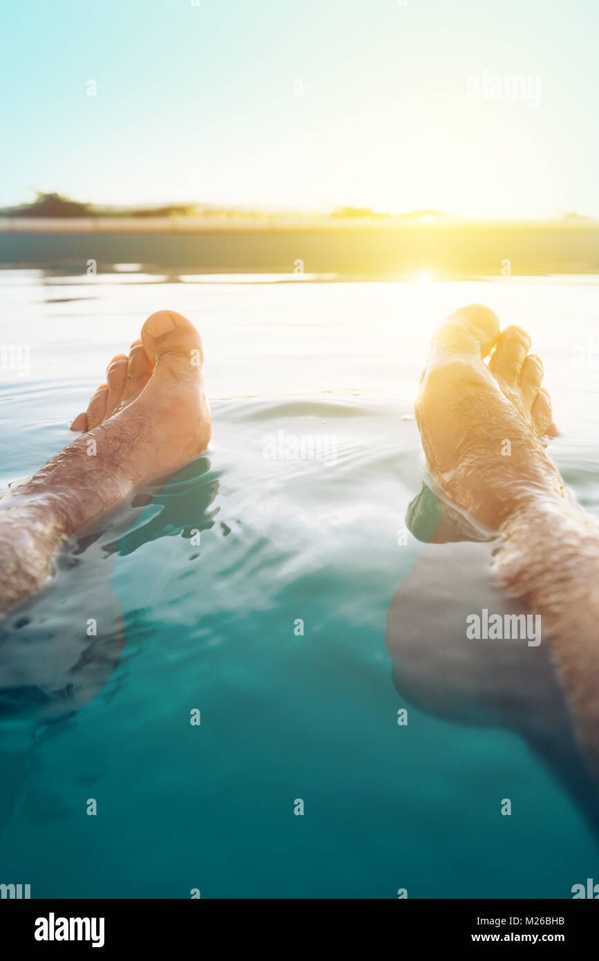 Männliche Füße im Außenpool. Mann genießen Sie erfrischende Pool Wasser im Sommer Sonnenuntergang. Ferien und Wochenende. Stockfoto