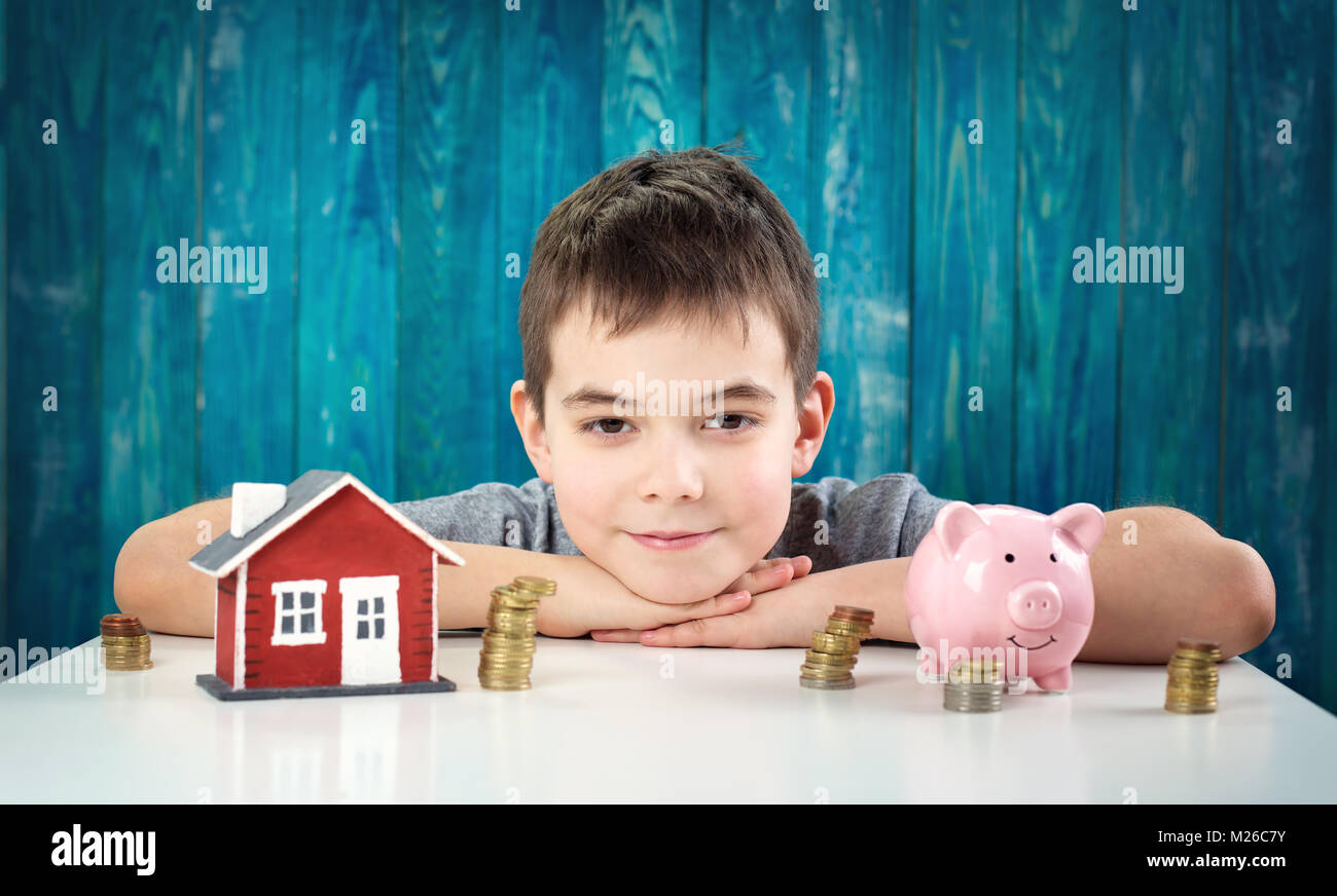 Acht Jahre altes Kind mit am Tisch sitzen und ein sparschwein Stockfoto