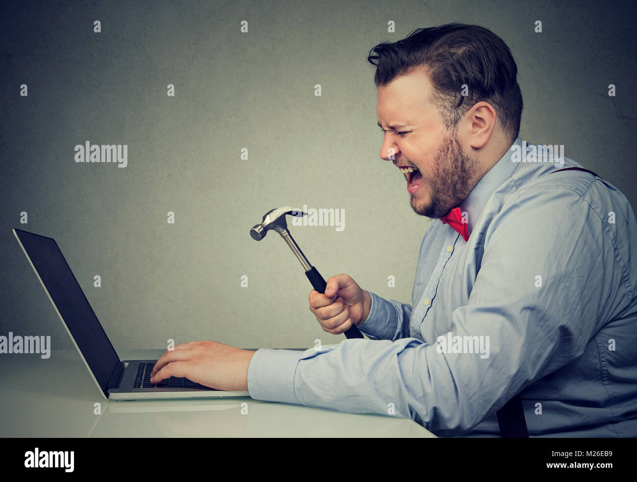 Jungen zornigen Mann frustriert mit defekten Laptop und Holding Hammer bereit, es zu vernichten. Stockfoto