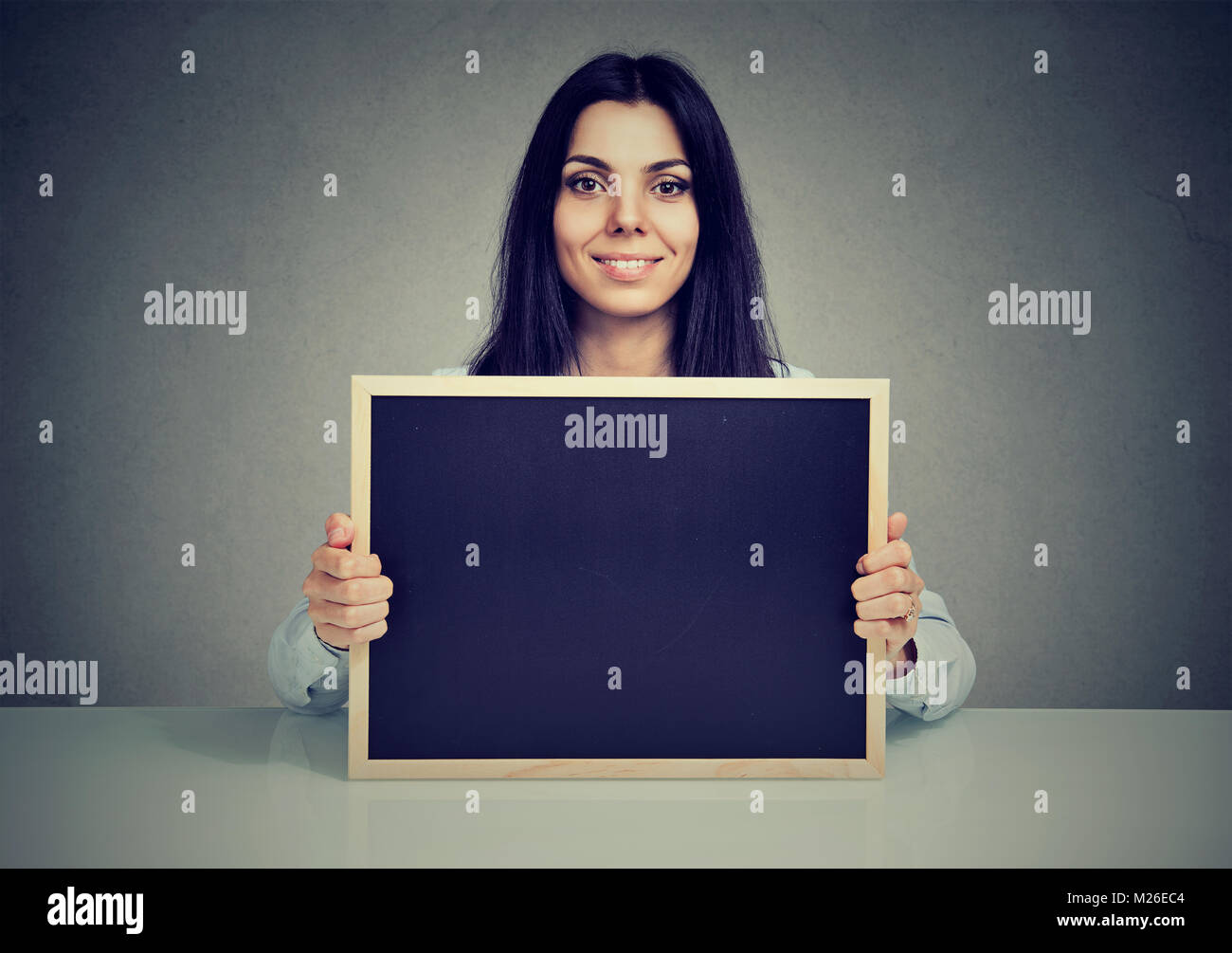 Junge Frau sitzt und zeigt leere Tafel an der Kamera schaut. Stockfoto