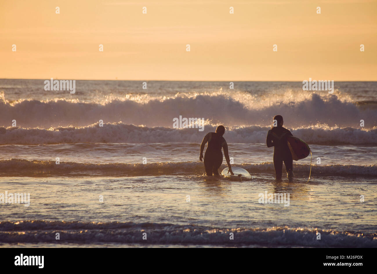 Wellenreiten an der Baskischen Küste in Anglet, an einem Abend vor Sonnenuntergang. Zwei junge Frauen aus hinter Fuß in Richtung der Wellen gesehen Stockfoto