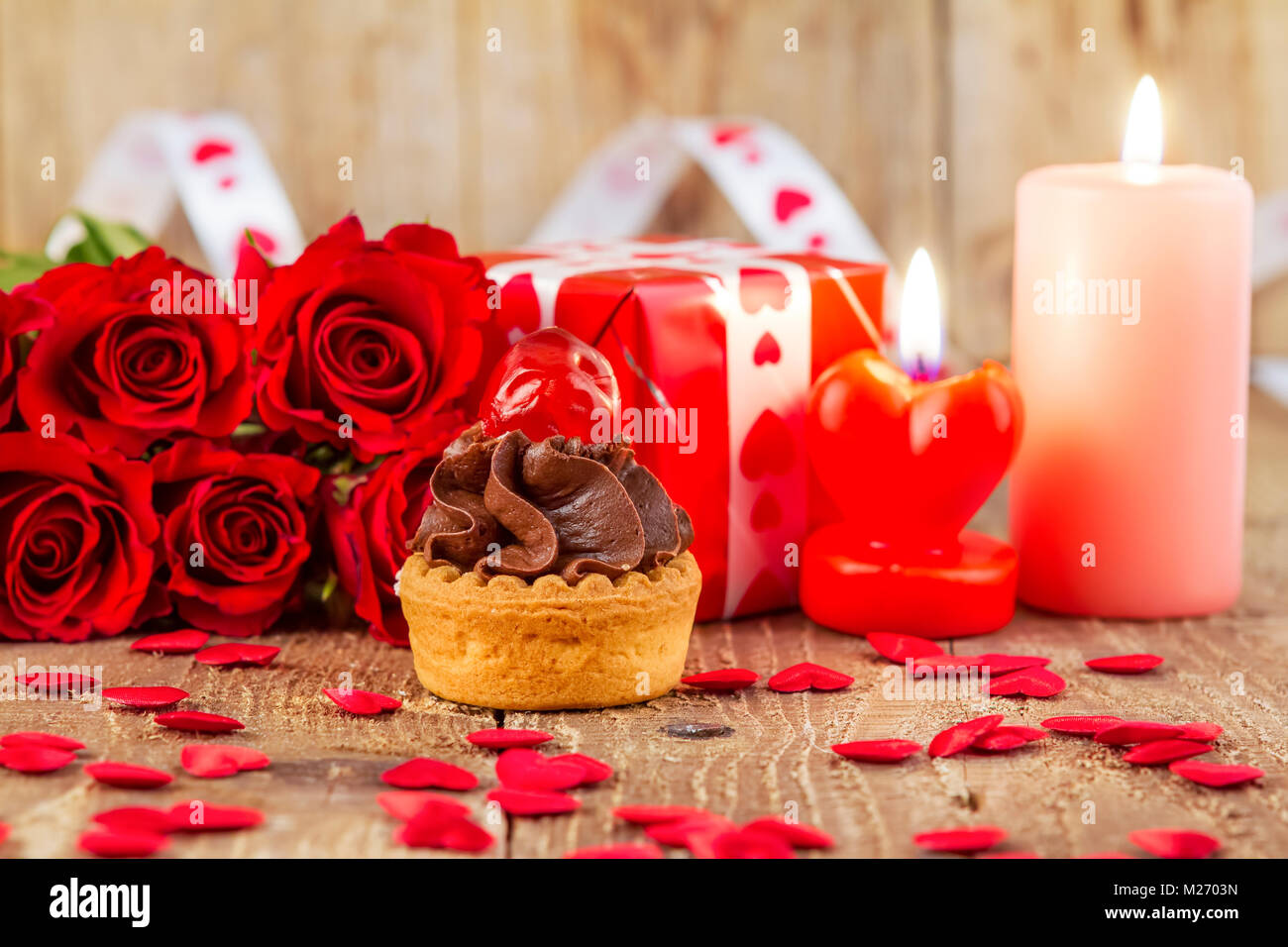 Cupcake mit Cherry vor Strauß roter Rosen und Kerzen auf Holz- Hintergrund. Valentines Tag Konzept. Fokus auf Kuchen! Stockfoto