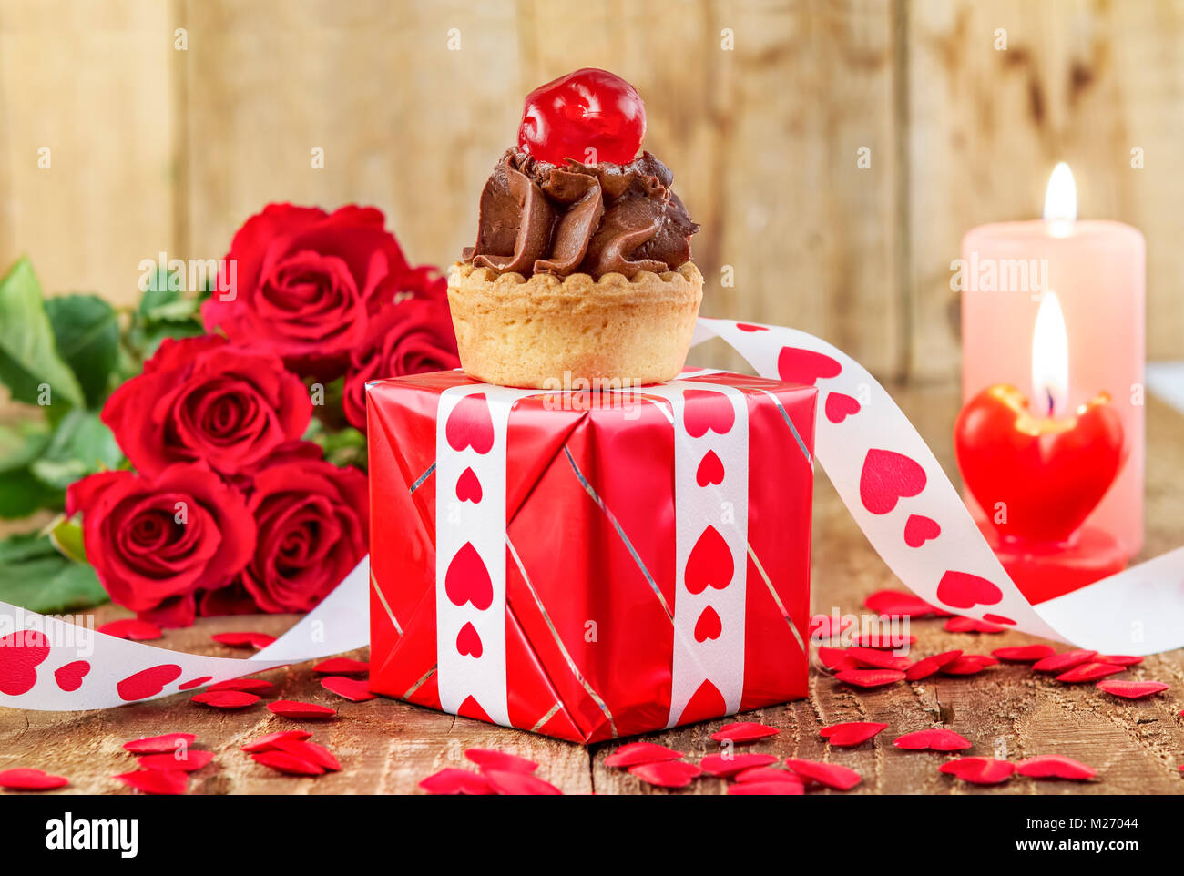 Cupcake mit Cherry in roter Geschenkbox vor Strauß roter Rosen und Kerzen auf Holz- Hintergrund. Valentines Tag Konzept. Muttertag Konzept! Stockfoto