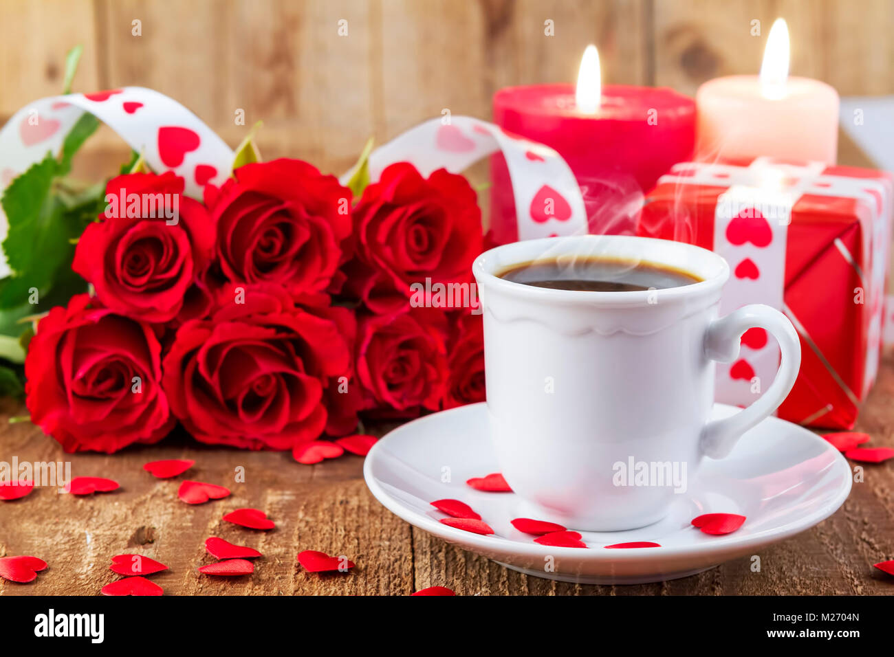 Tasse mit Kaffee vor Strauß roter Rosen und Kerzen auf Holz- Hintergrund. Valentines Tag Konzept. Happy Mother's Day Konzept! Fokus auf Tasse Stockfoto