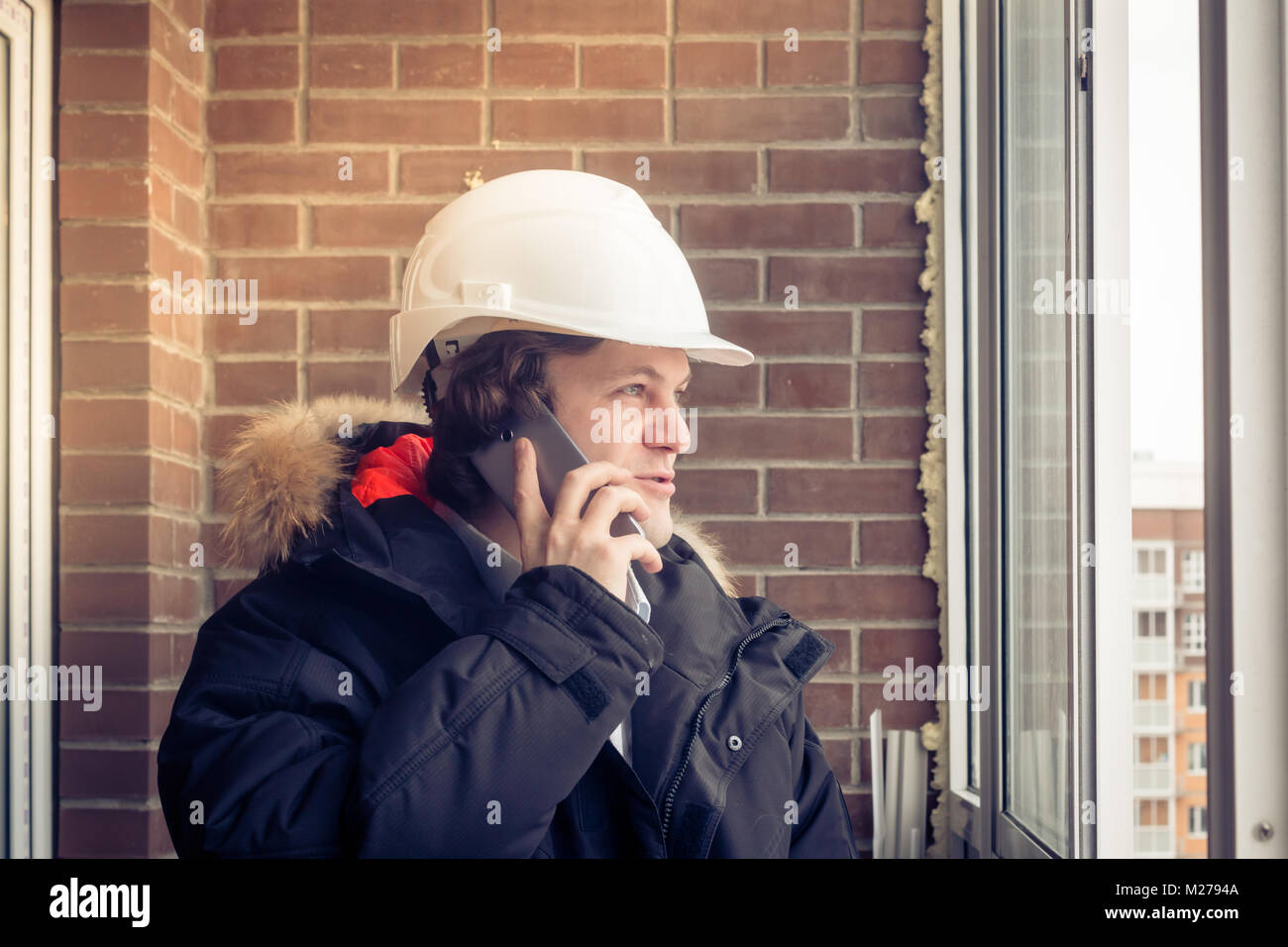 Junge Bauingenieur Probleme über das Telefon gegen Ziegel Hintergrund. Soft Focus, getönt. Stockfoto