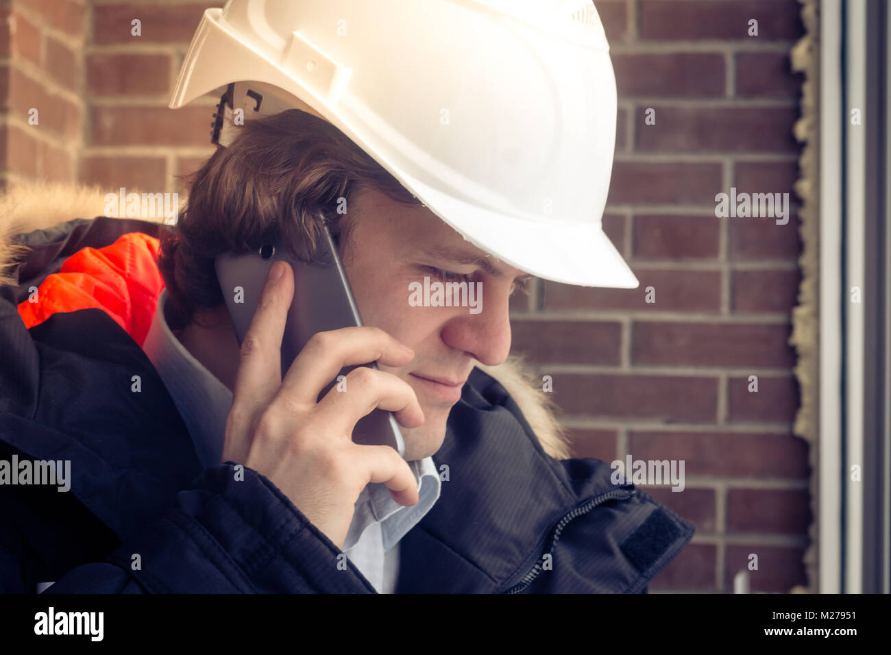 Bau Inspektor im weißen Helm Gespräch am Handy auf dem braunen Mauer Hintergrund. Soft Focus, getönt. Close Up. Stockfoto