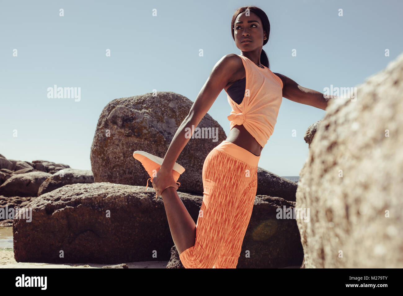 Gesunde Frau, die von einem Felsen und Strecken die Beine vor der Ausführung am Meer. Läuferin dabei warm-up Routine am Strand vor dem Ausführen, stretchin Stockfoto