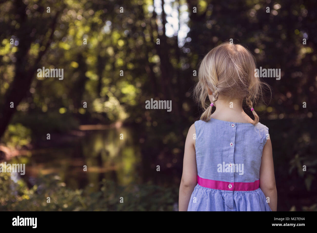 Kleine Mädchen stehen in der Betrachtung und der Suche nach einer ruhigen, bewaldeten Fluss Stockfoto