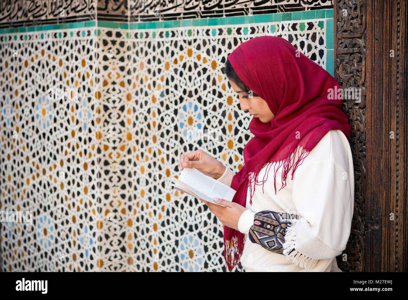 Arabische Frau in traditioneller Kleidung mit roten Kopftuch auf dem Kopf ein Buch lesen Stockfoto