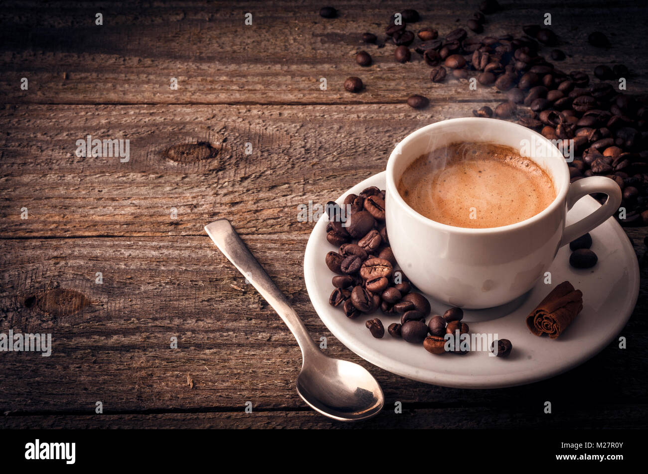 Eine Tasse Kaffee auf alten hölzernen Tisch mit ein paar Bohnen einen Löffel und eine Stange Zimt Stockfoto