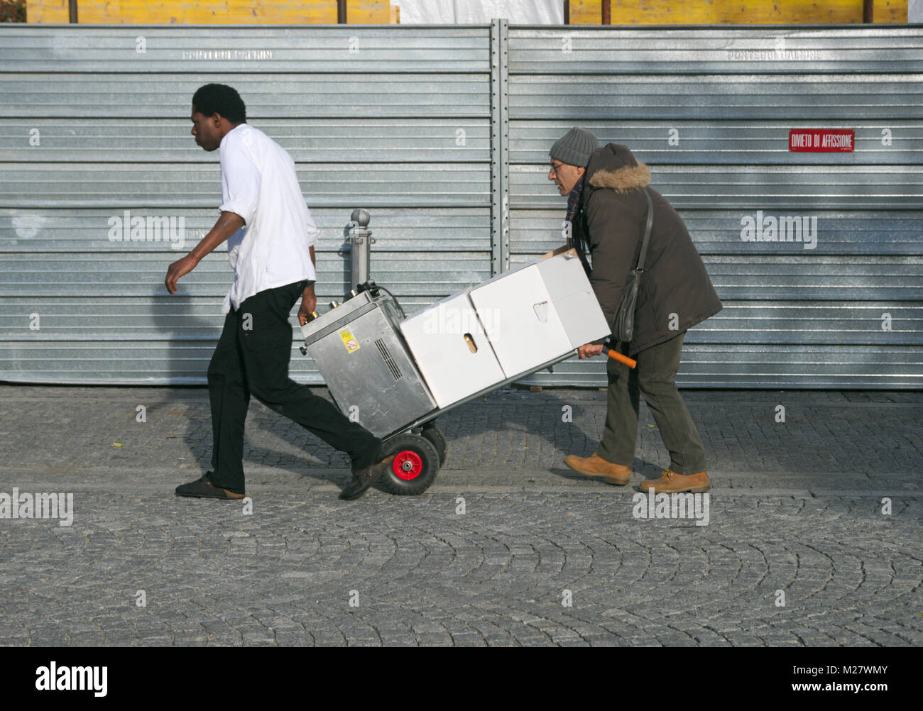 Männer ziehen geladen Warenkorb auf der Straße, Mailand, Italien Stockfoto