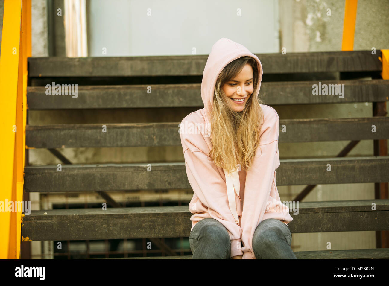 Coole hipster junge Frau in Rosa hoodie auf einige gelbe Treppen, warten, Spielen, frei zu sein, Stockfoto