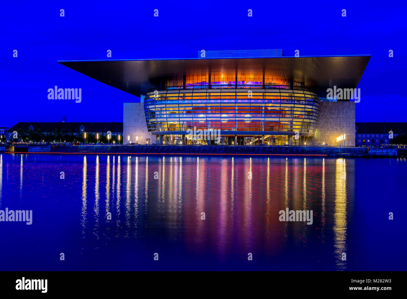 Blaue Stunde Kopenhagen Dänemark mit Hafenblick Oper leuchtet am Ocean widerspiegelt. Leichte Spuren von Boot in Rot im Vordergrund. Stockfoto