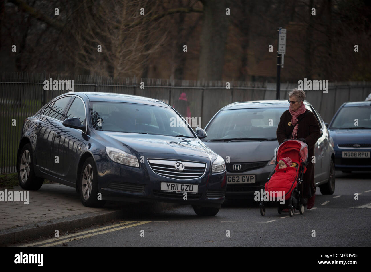 Eine ältere Dame mit einem Kind buggy Spaziergänge in der Straße eine geheimnisvoll verlassenen Vauxhall Auto bei 45 Grad ausruhen, weg von der Straße, sondern blockieren eine Plasterung an Ruskin Park, am 2. Februar 2018, in Southwark, London, England. Denn das Auto ist nicht die Autobahn blockieren, ist dies nicht der Polizei Sache - aber wodurch ein Hindernis auf der Fahrbahn macht es zu einem Rat problem. Stockfoto