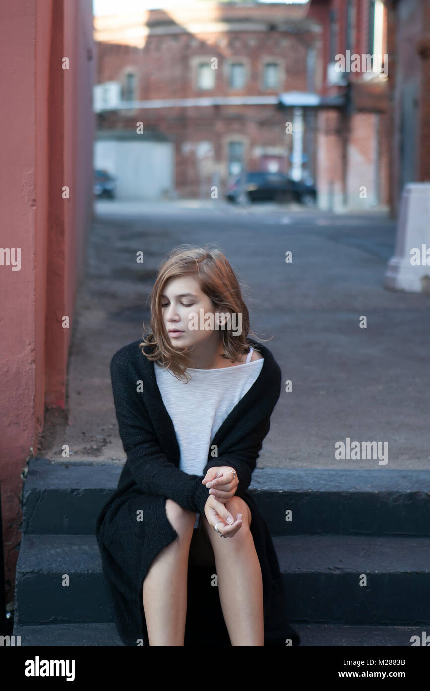 Eine nachdenkliche Mädchen in einem lange schwarze Strickjacke und kurzen Shorts sitzt auf den Stufen Stockfoto Eine nachdenkliche Mädchen in einem lange schwarze Strickjacke und kurzen Shorts sitzt auf den Stufen Stockfoto