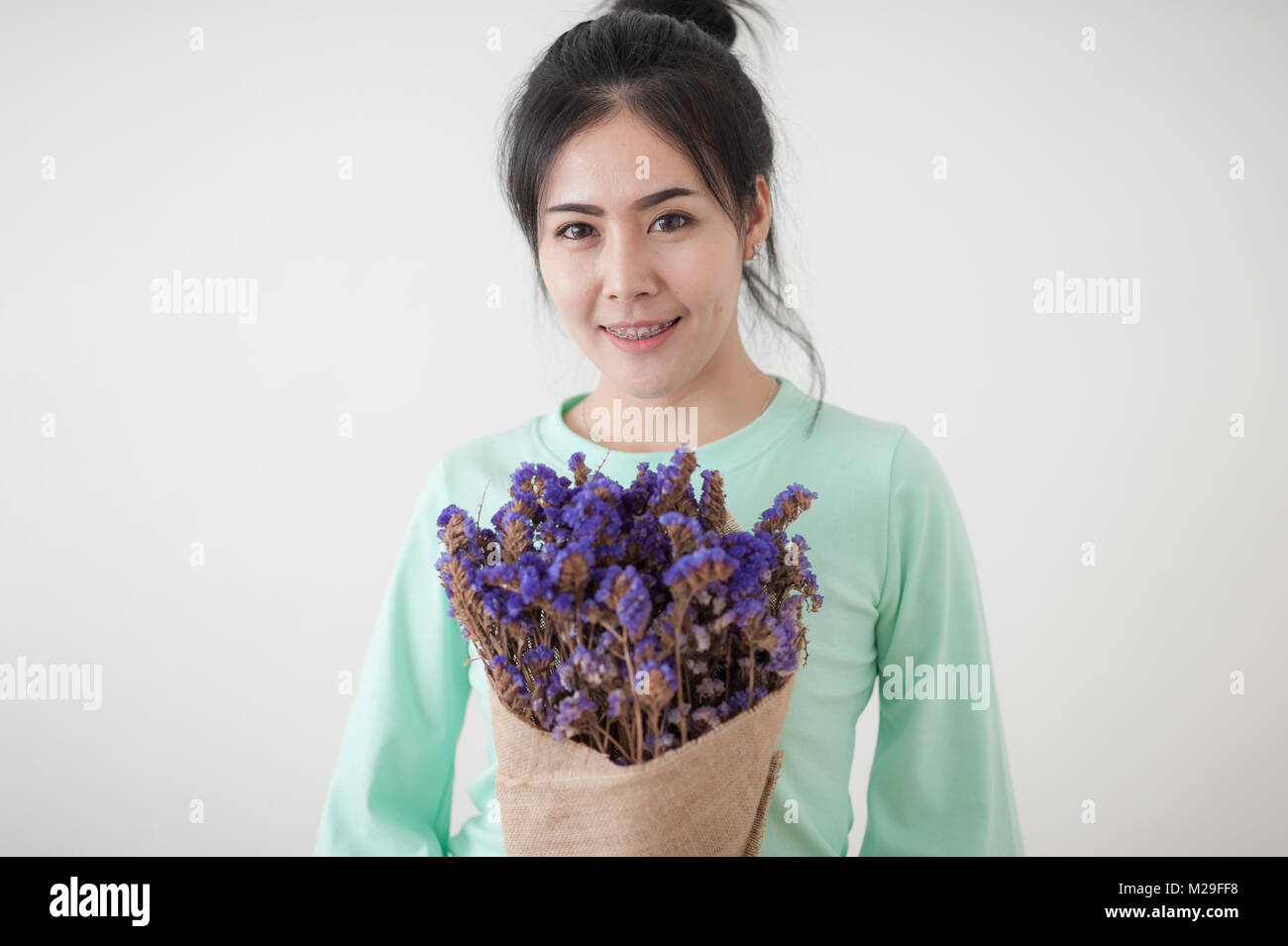 Junge schöne asiatische Frau in Grün shirt halten Sie die Blumen in den Händen am Morgen Zeit mit natürlicher Beleuchtung. Person Gestikulierte mit positiven emoti Stockfoto