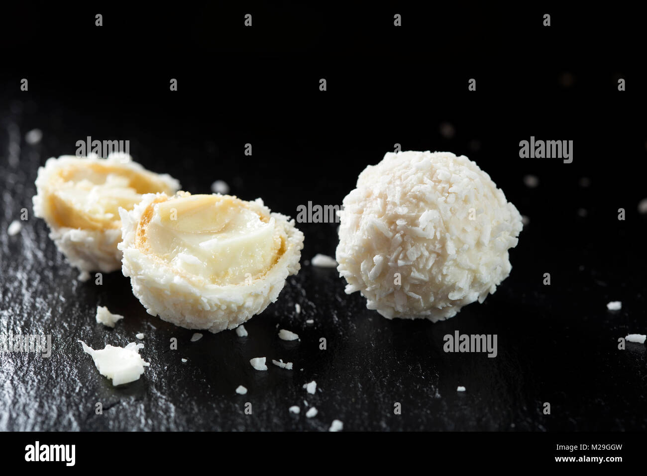 Gebrochene Raffaello weiße Süßigkeit mit Kokosraspeln auf einer Schiefertafel dunklen Hintergrund Stockfoto