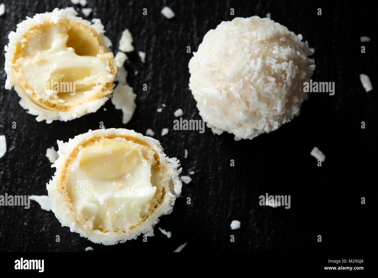 In der Nähe von Broken Raffaello weiße Süßigkeit mit Kokosraspeln auf einer Schiefertafel dunklen Hintergrund Stockfoto