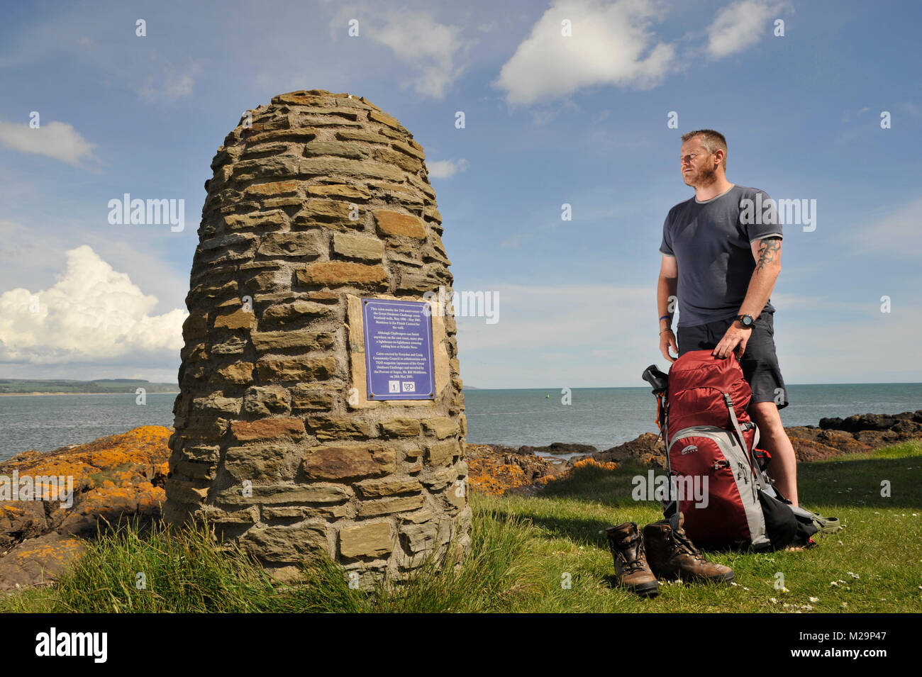 Ein Wanderer ruht seine müden Füße auf der großen Freien Herausforderung 25. Jahrestag Cairn an Scurdie Ness Licht Montrose, Angus, Schottland. Stockfoto