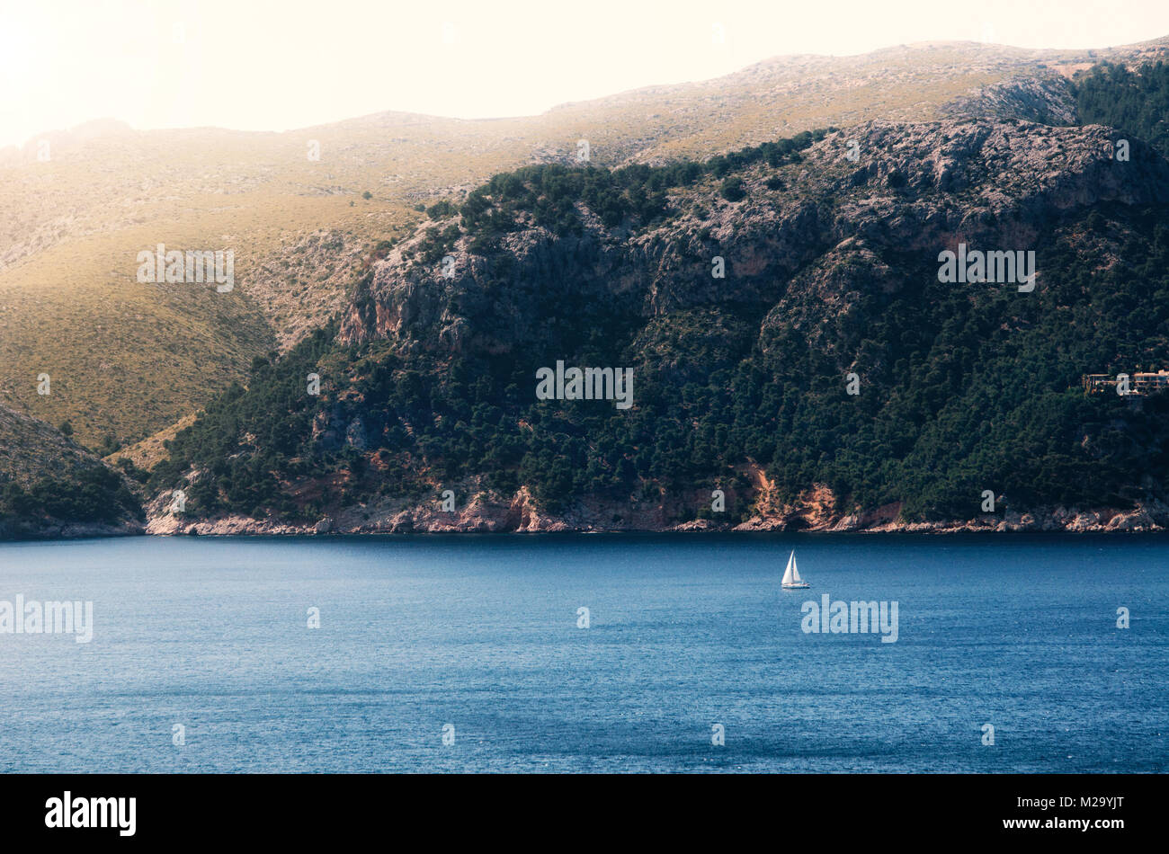 Mittelmeer Landschaft, Segelboot Segeln auf den Abstand auf majestätische Berge mit Wald Hintergrund, romantische Kreuzfahrt auf Mallorca, Spanien Stockfoto