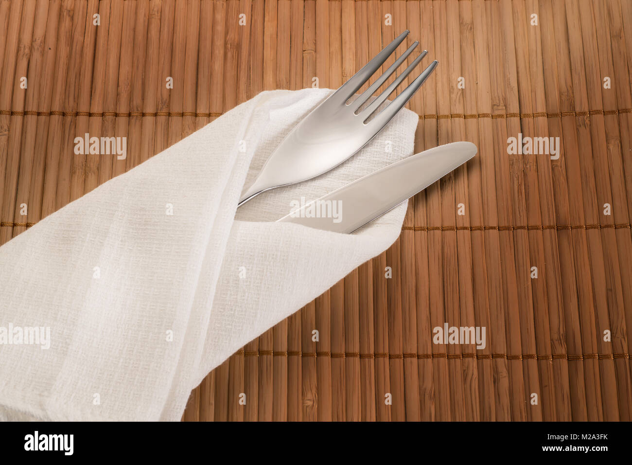 Einstellung statt. Messer und Gabel in Weiß textil Serviette auf beige Bambus Tisch Stockfoto