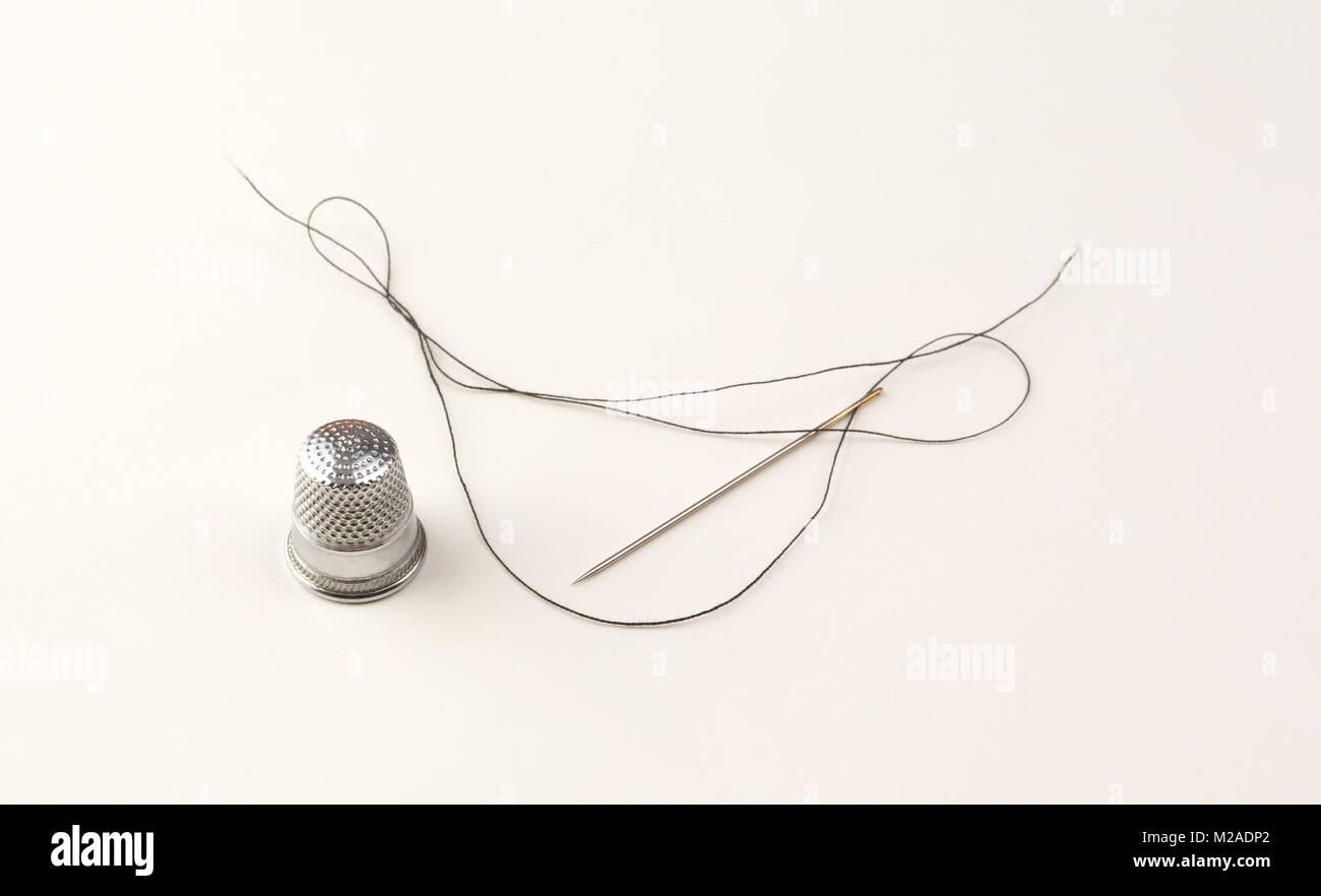 Eine alte Metall nähen Fingerhut und langen gewindeseite Nadel mit String auf weißem Papier. Stockfoto