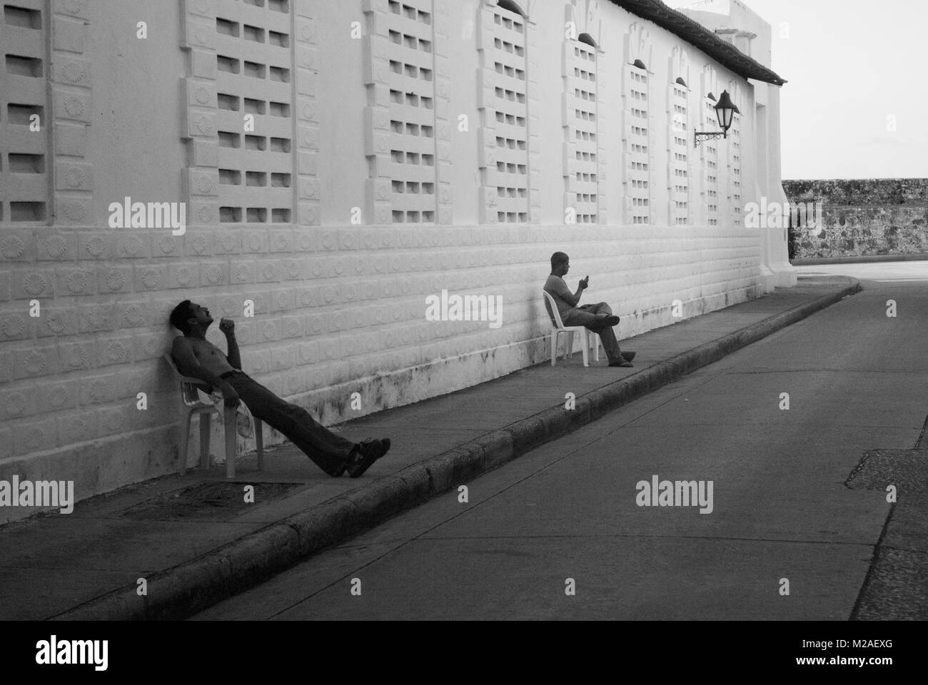 Zwei Männer sitzen auf Stühlen in einer Straße in Cartagena, Kolumbien Stockfoto