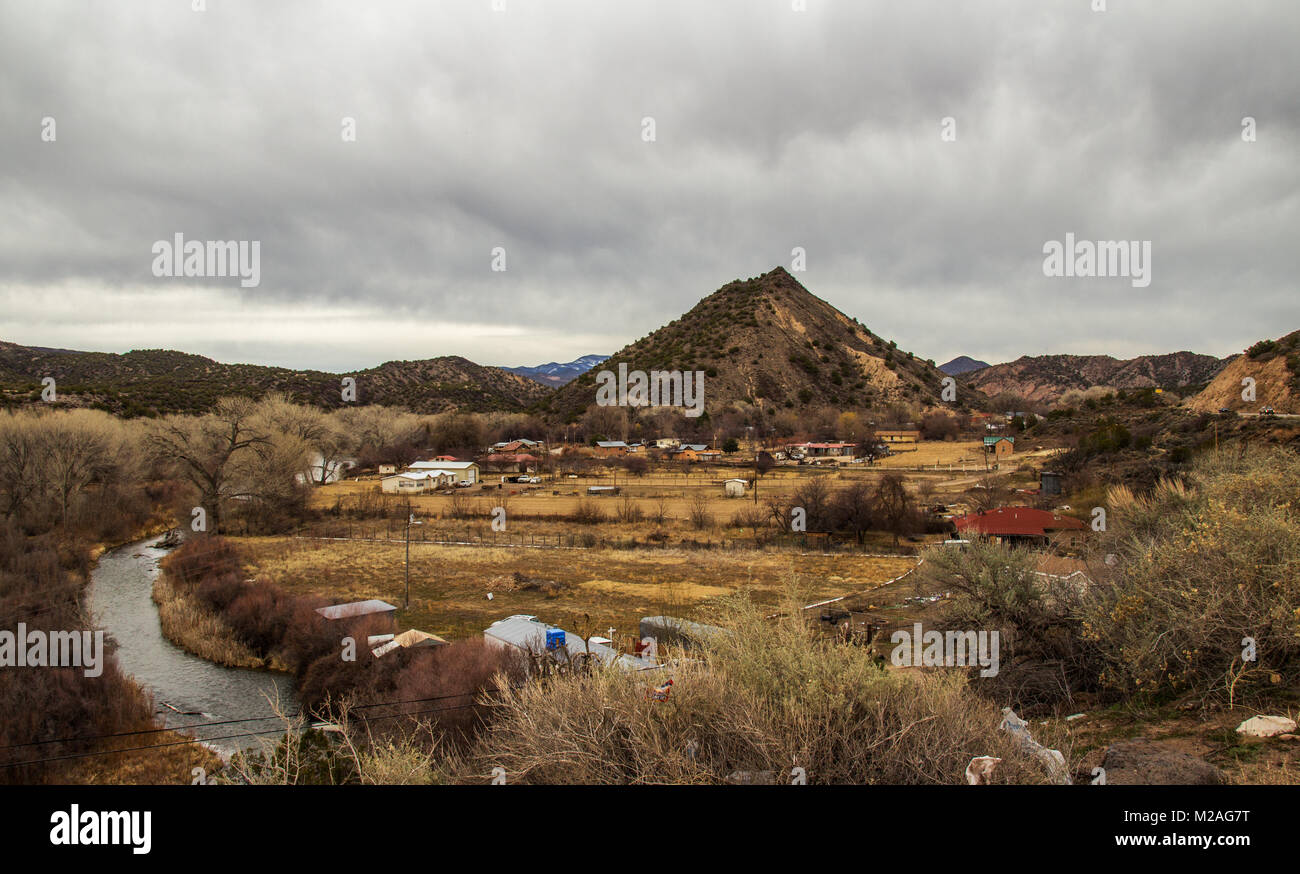 Ein kleines Dorf umgeben von felsigen Bergen, bestreut mit Sträuchern in einem bewölkten Frühling Landschaft in Neu Mexiko umgeben Stockfoto