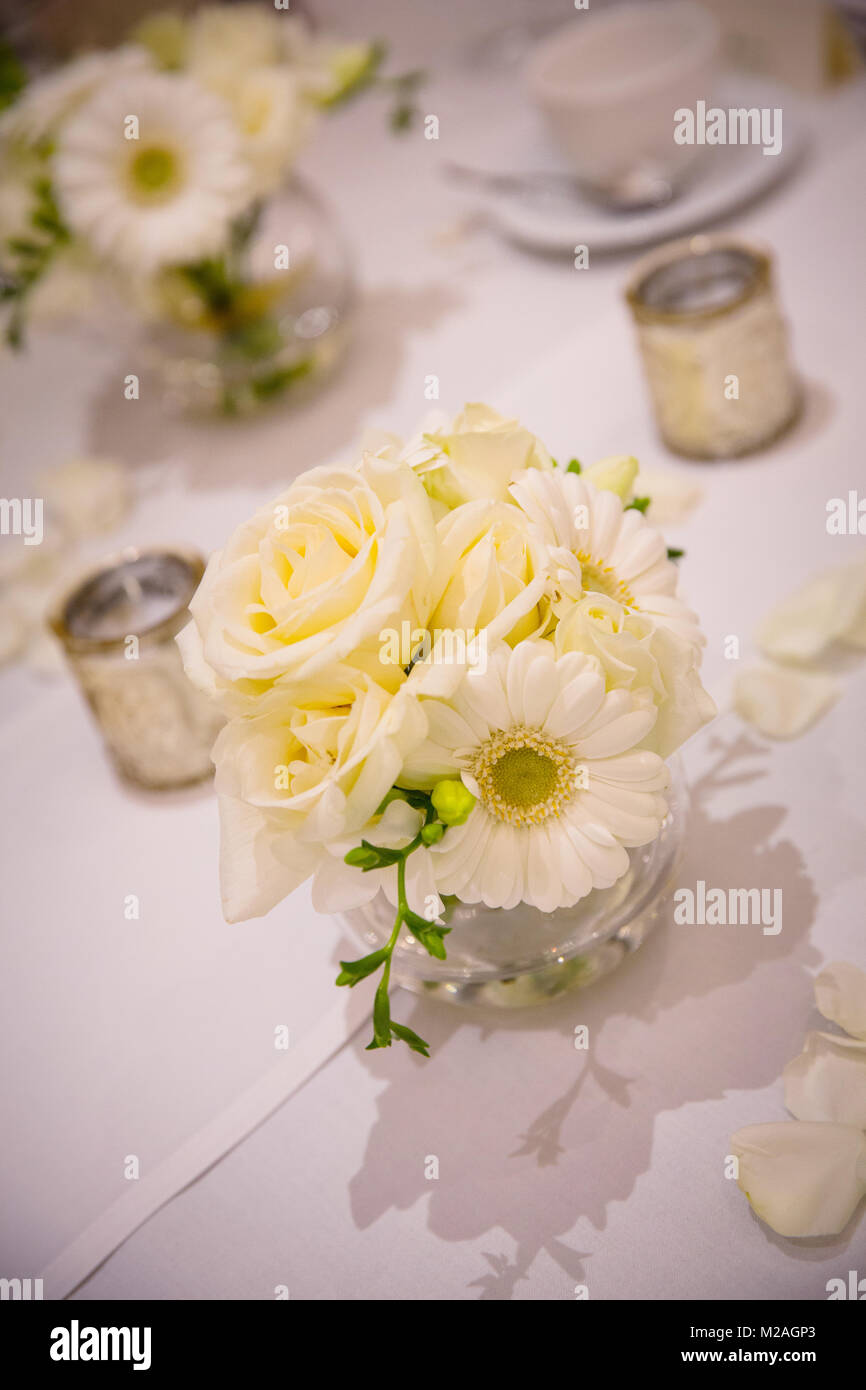 Blumenschmuck auf der weißen Tischdecke mit Rosenblättern Stockfoto