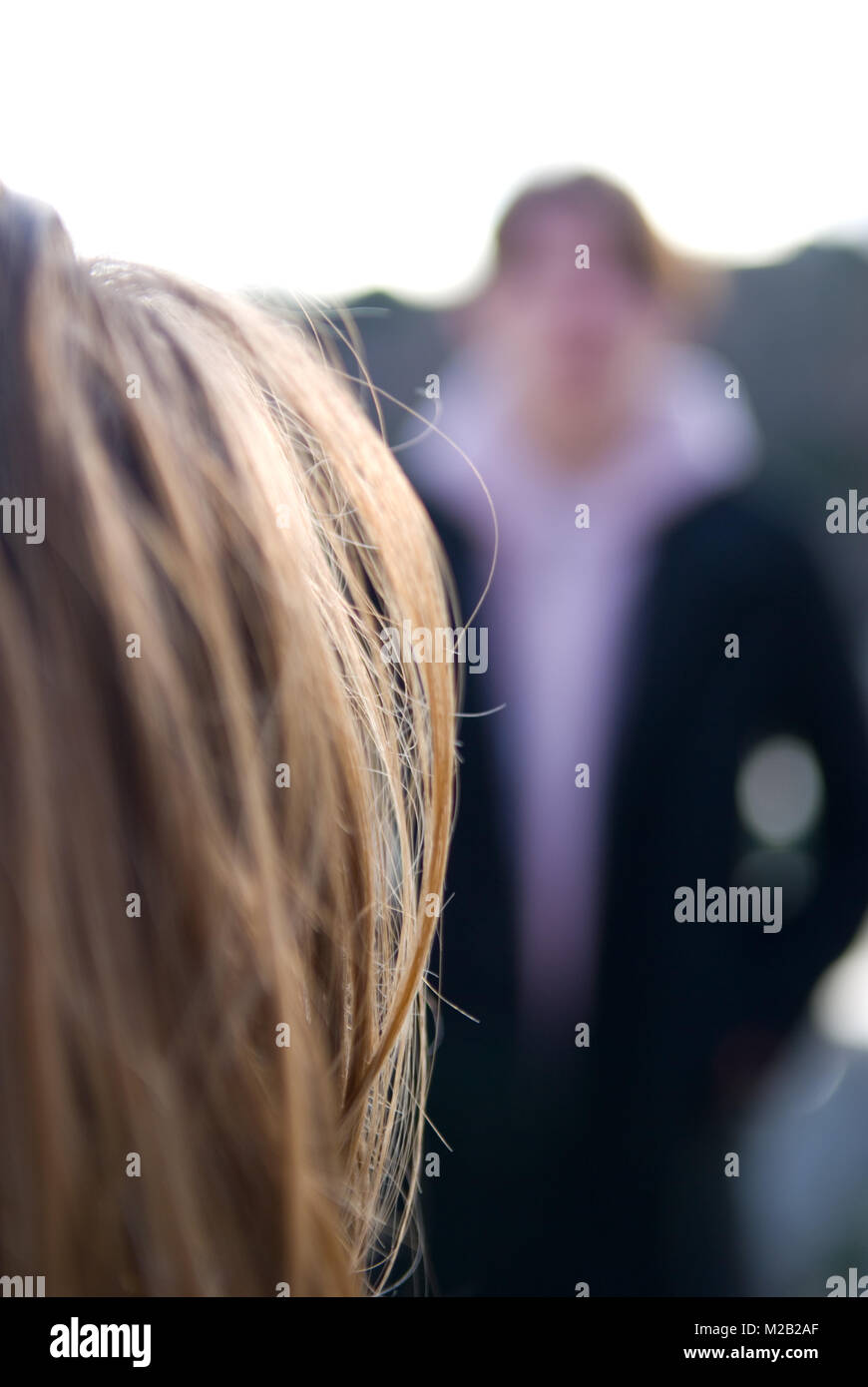 Makro Detail Schoß der Frau haar scharf in den Vordergrund mit unscharfen Mann stand mit hnads in Taschen im Hintergrund Stockfoto