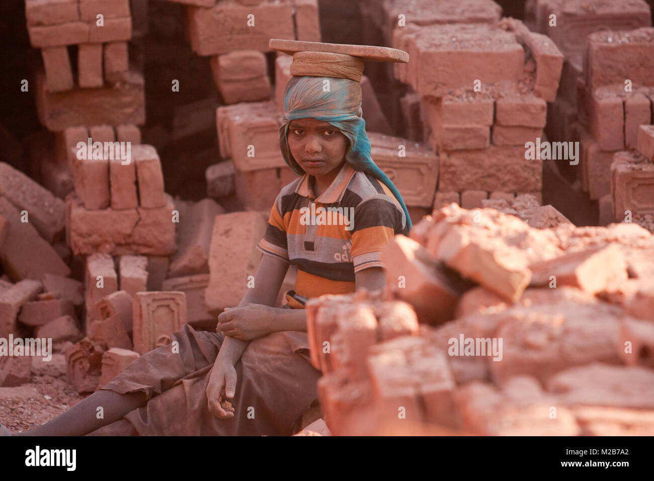 Ein kleiner Junge liegt beim Tragen von Steinen aus dem Brennofen, um den Stapler in Bhaktapur, Nepal. Stockfoto