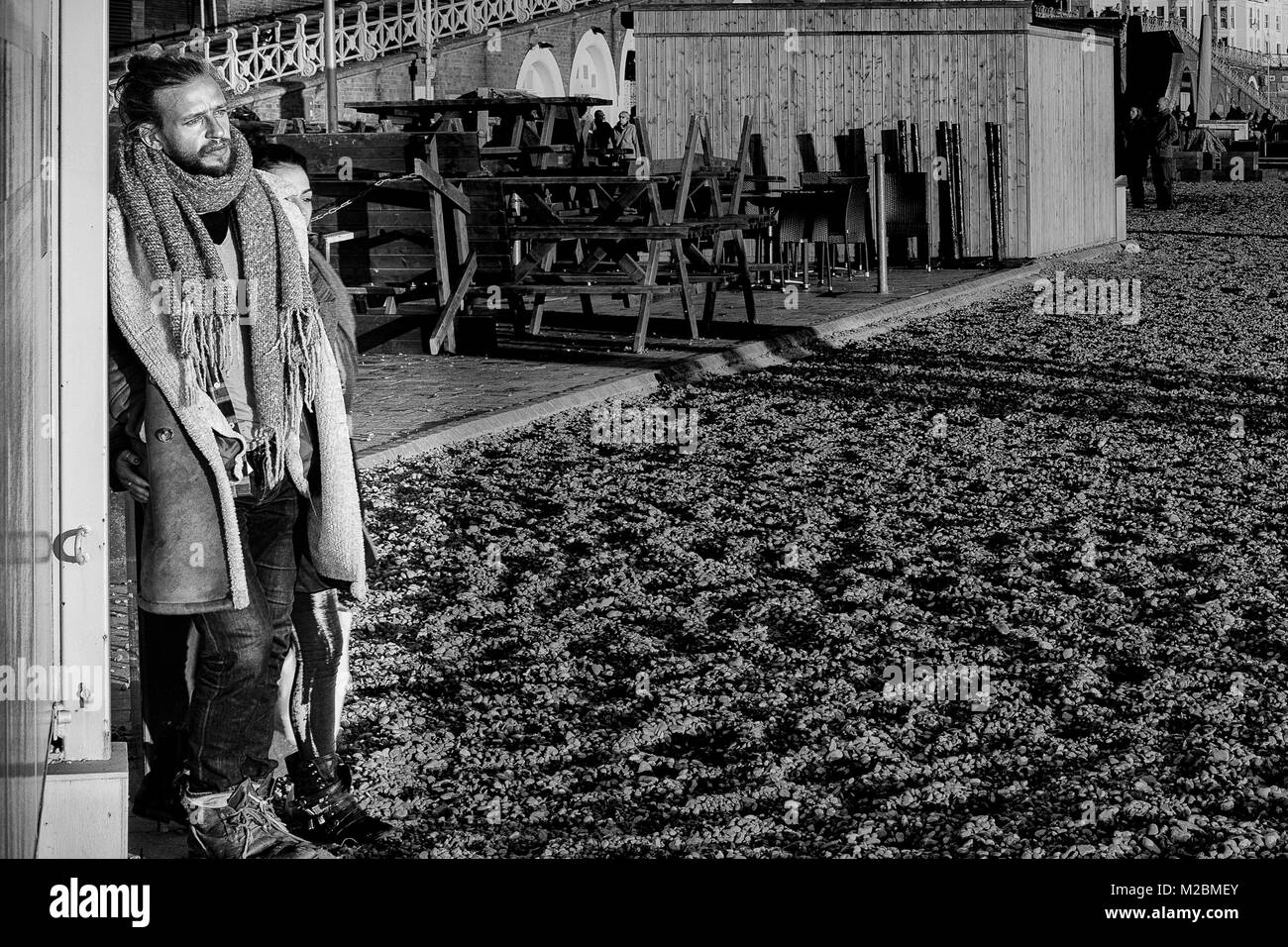 Männliche gegen eine Wand an Brighton Beach lehnend, im Winter in Schwarz & Weiß Stockfoto