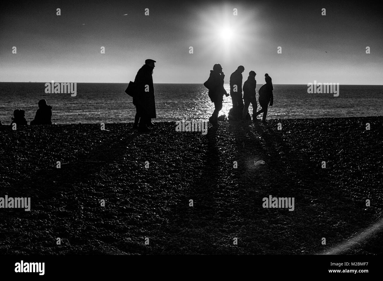 Silhouetten, die auf Brighton Beach im Winter mit der Sonne hinter Stockfoto