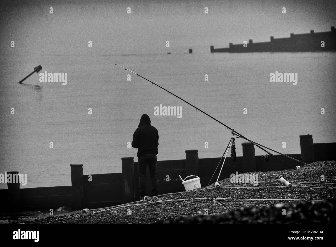 Einsamer Strand Fischer im Winter auf einem britischen Strand, in Schwarz und Weiß Stockfoto
