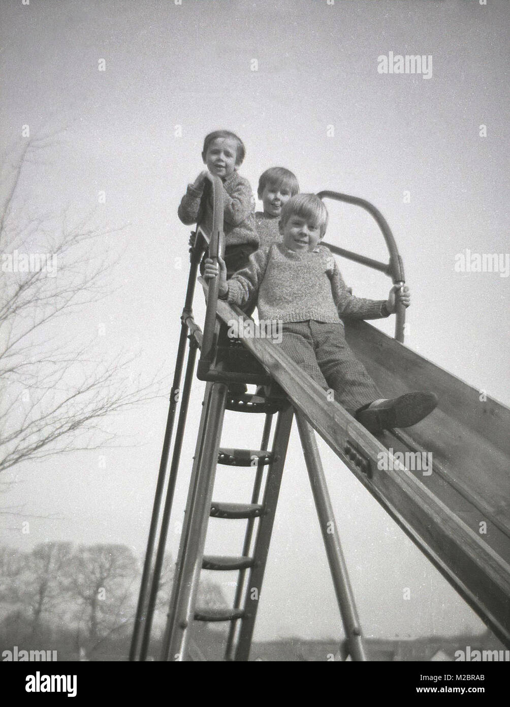 1960, historische, drei kleine Jungen zusammen, alle Brüder, und tragen die gleichen gestrickte Pullover, schauen Sie von oben nach unten aus einem Metall Rutschbahn, England, UK. Stockfoto