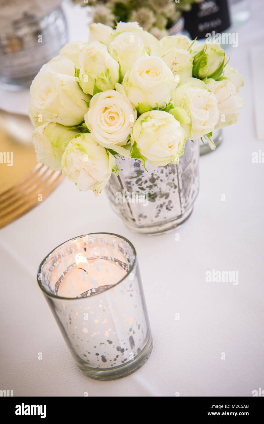 Blumenschmuck in der Vase auf dem Tisch, mit Kerzenlicht im Vordergrund Stockfoto